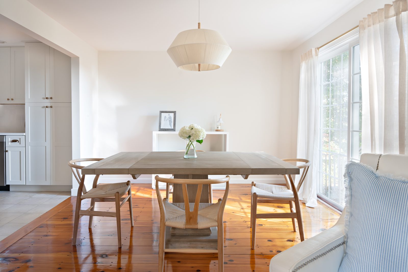 Indian Road dining room with wishbone chairs, square wood table, linen pendant, and pine floors