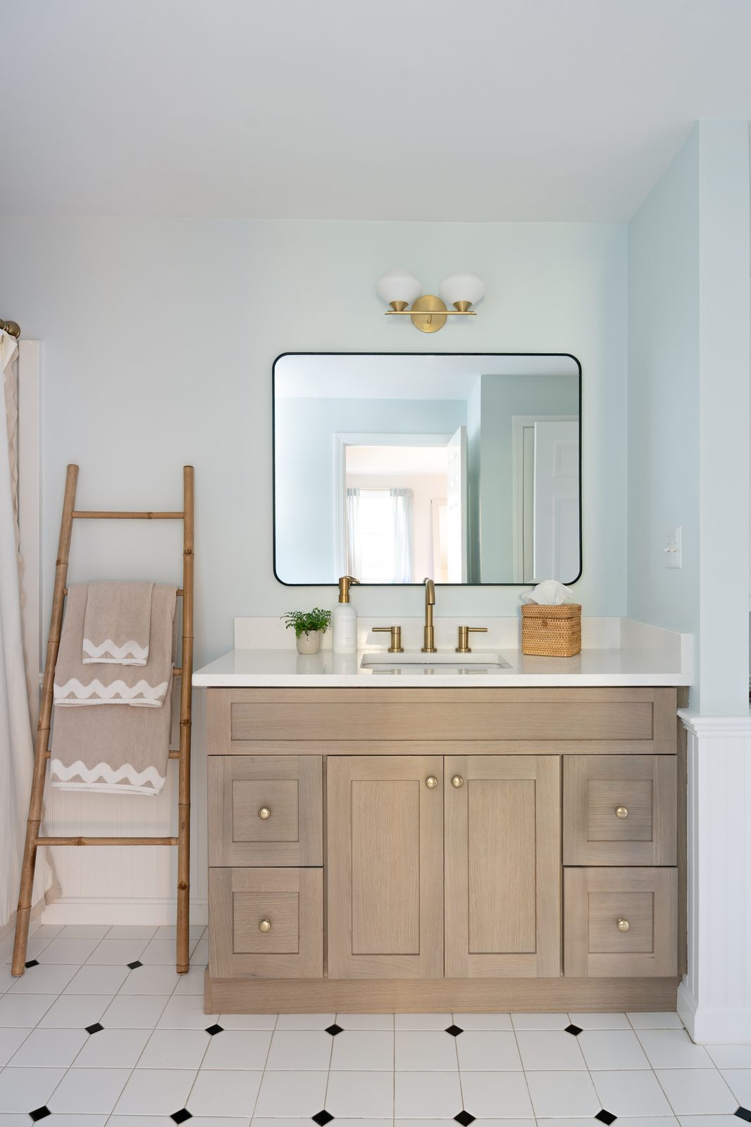 Indian Road bathroom with light oak vanity, brass fixtures, black-framed mirror, and black-and-white hex tile floor