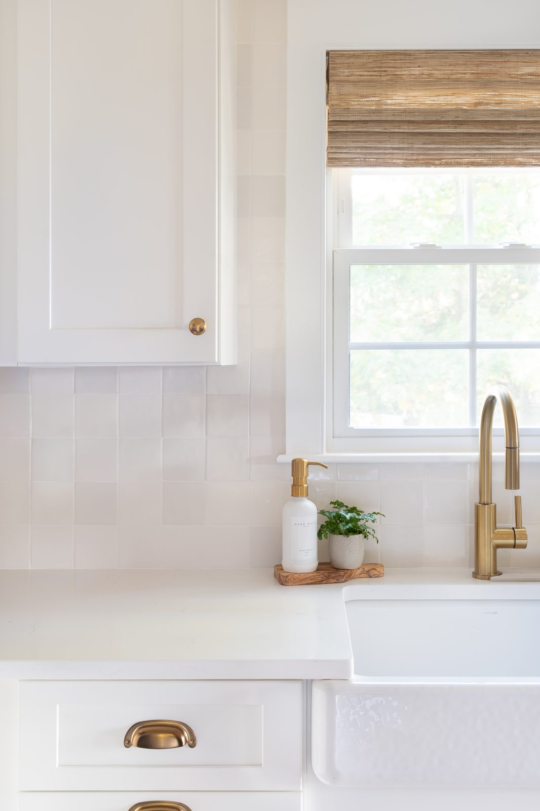 Indian Road kitchen sink detail with white zellige tile backsplash, farmhouse sink, brass faucet, and woven roman shade