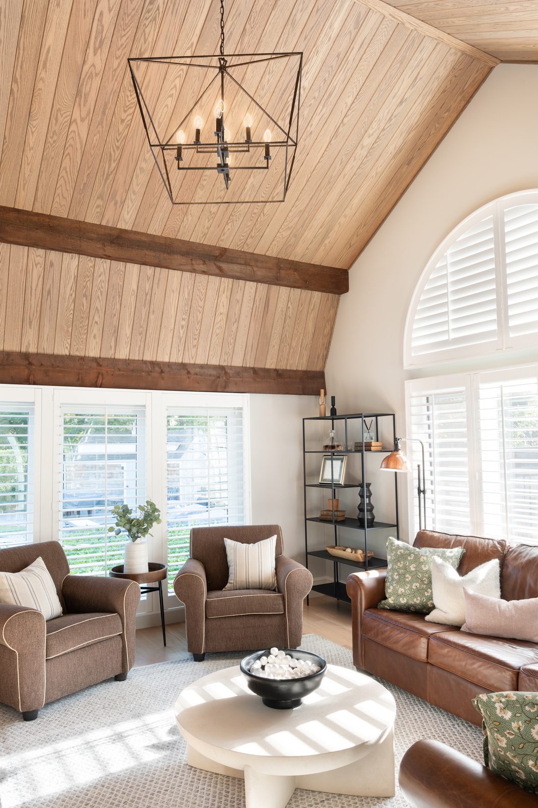 Jerusalem Road living room — wide view with vaulted ceiling, arched window, leather sofa, and upholstered chairs