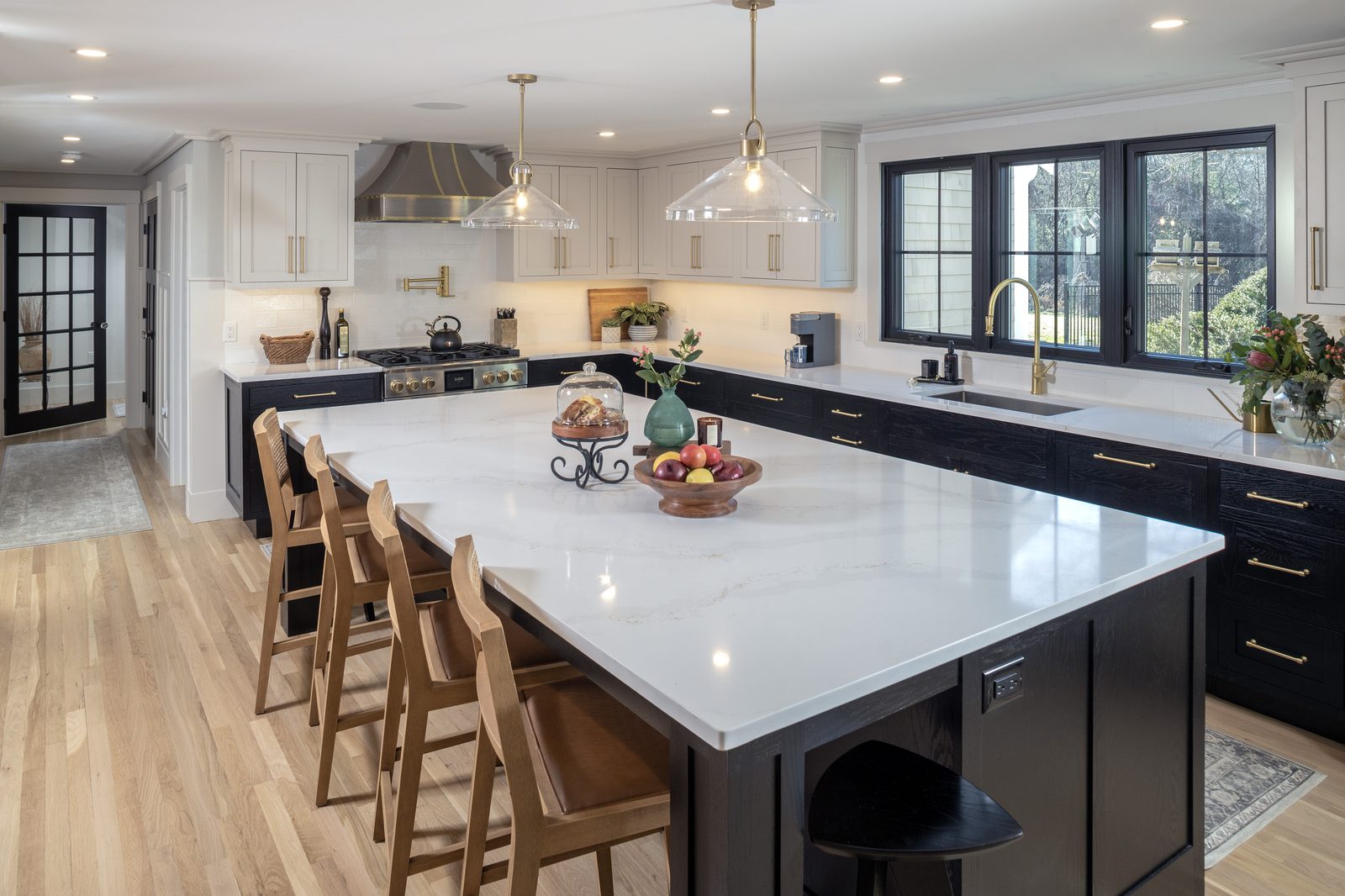 Main Street kitchen with black lower cabinetry, white upper cabinets, oversized white quartz island, and brass hardware