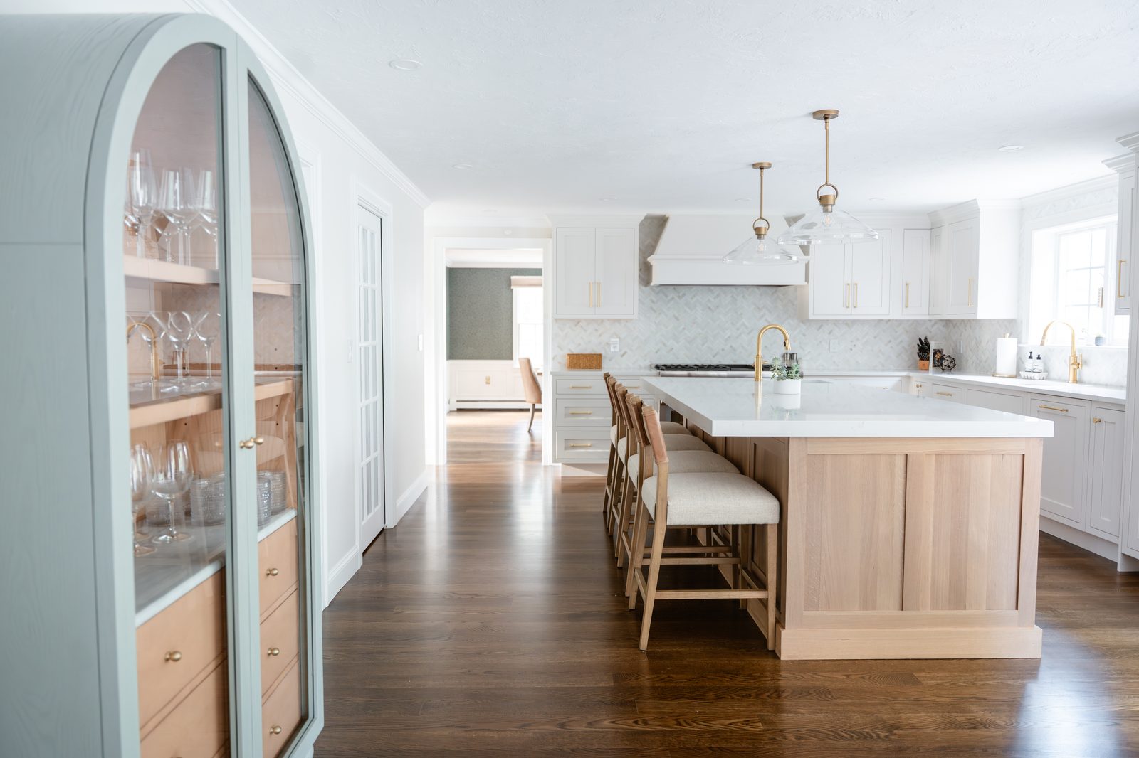 Rosewood Court kitchen with arched sage glass cabinet, white oak island, marble herringbone backsplash, and brass pendants